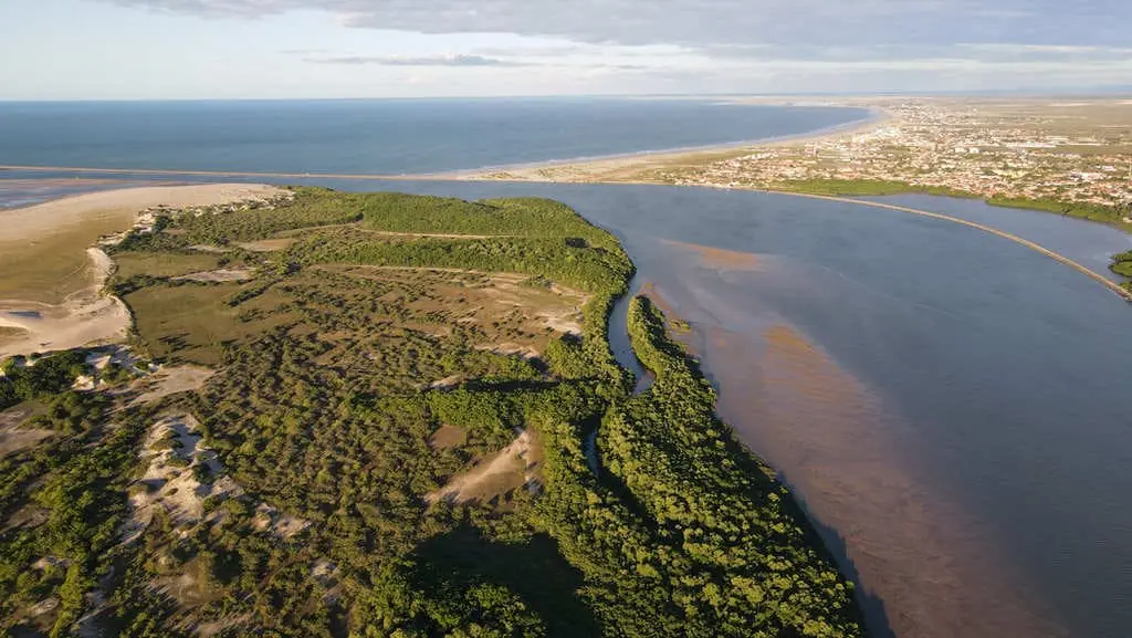Vista aérea de faixa de vegetação e dunas entre o rio e o mar, com uma cidade ao fundo na região do Delta do Parnaíba