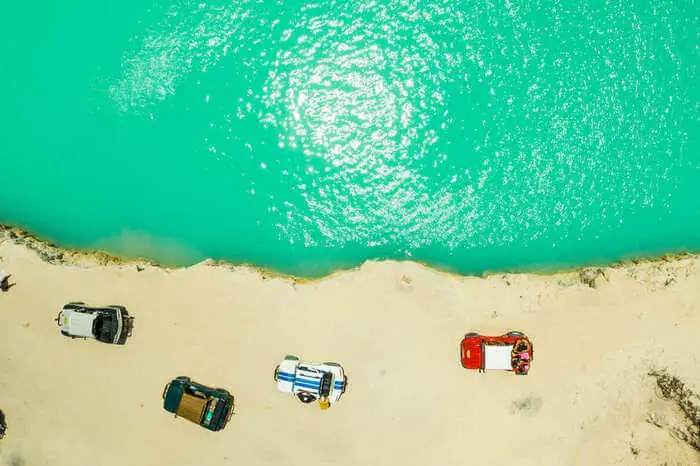 Vista aérea de buggies e jipes estacionados na areia à beira de uma lagoa verde-turquesa