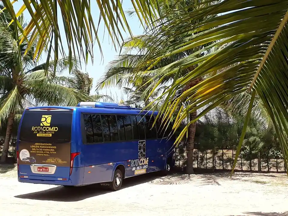 Micro-ônibus azul da Rota Combo estacionado na areia sob coqueiros