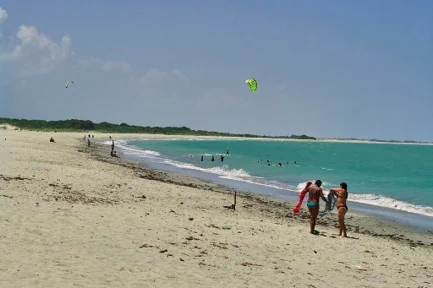 Banhistas e pipas de kitesurf sobre o mar verde-azulado da Praia de Barra Grande, no Piauí