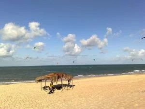 Pipas de kitesurf sobre o mar da Praia de Cumbuco, com guarda-sol de palha na areia