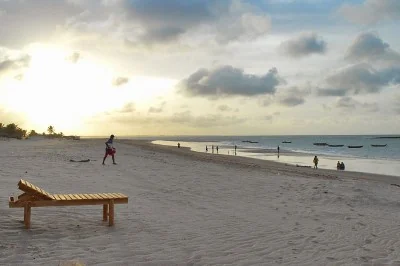 Espreguiçadeira de madeira na areia e pessoas caminhando na Praia do Coqueiro ao entardecer